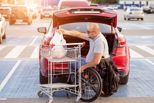 La persona con discapacidad física pone las compras en el maletero de un automóvil en el estacionamiento de un supermercado.