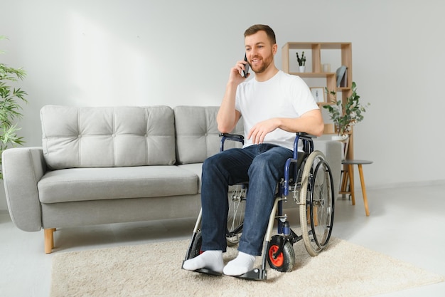 La persona discapacitada se sienta en una silla de ruedas Está hablando con alguien en su teléfono inteligente Está en su gran salón luminoso Sonríe