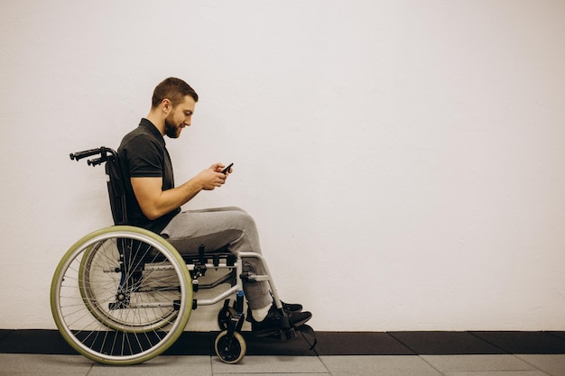 La persona discapacitada se sienta en una silla de ruedas Está hablando con alguien en su teléfono inteligente Está en su gran salón luminoso Sonríe