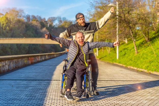 Persona discapacitada en silla de ruedas con un amigo feliz sonriendo disfrutando con los brazos arriba vistoria disfrutando de la vida al atardecer de la ciudad