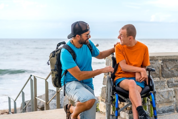 Una persona discapacitada en silla de ruedas con un amigo en vacaciones de verano hablando junto al mar