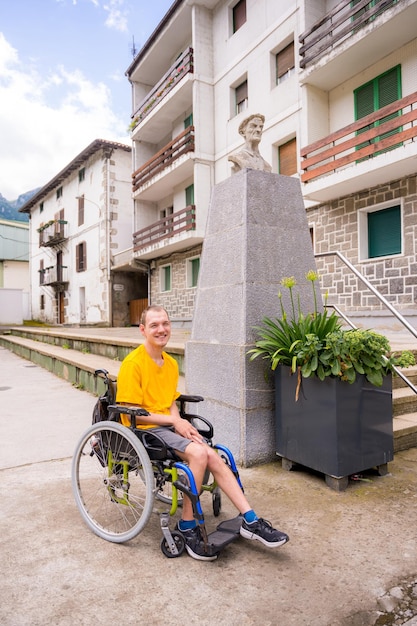 Una persona discapacitada en silla de ruedas junto a una escultura en la plaza del pueblo