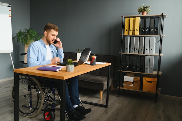 Persona discapacitada en silla de ruedas trabaja en la oficina en la computadora Está sonriendo y apasionado por el flujo de trabajo