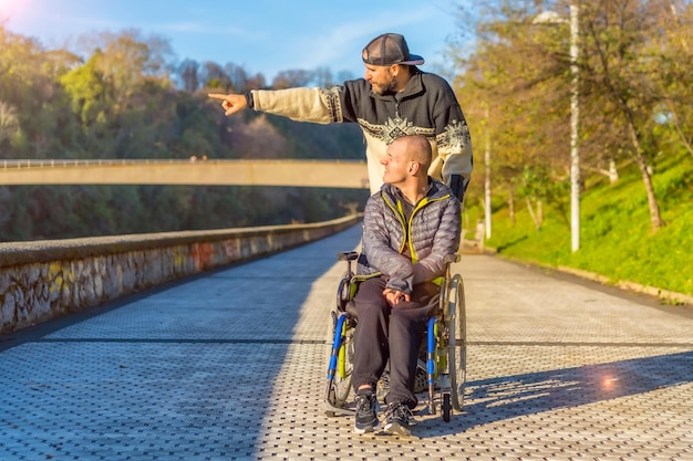 Persona discapacitada sonriente en silla de ruedas caminando con su hermano en un parque al atardecer