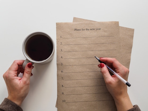 Persona escribiendo planes para el nuevo año mientras toma café