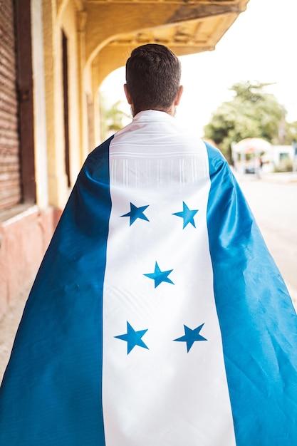 Una persona de espaldas caminando con una bandera de honduras encima Celebración del 15 de septiembre