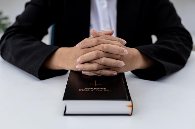 Una persona está poniendo sus manos juntas sobre el libro de la Biblia, está orando a la Biblia, está leyendo y estudiando la Biblia. Concepto de cristianismo y estudio de la Biblia.