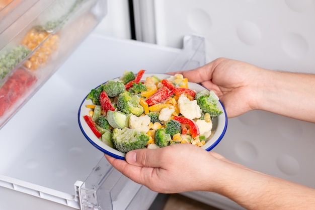 Una persona está sacando un plato de verduras congeladas del congelador de la nevera. Concepto de alimentos congelados, productos de almacenamiento a largo plazo.