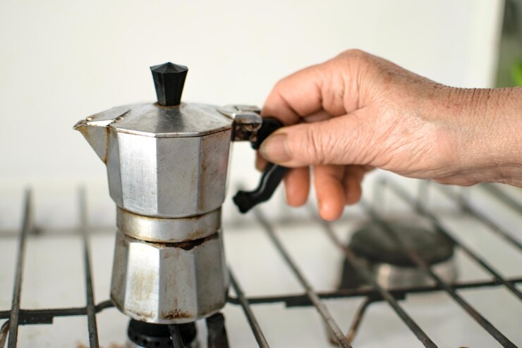 Una persona está usando una cafetera para verter café en una estufa.