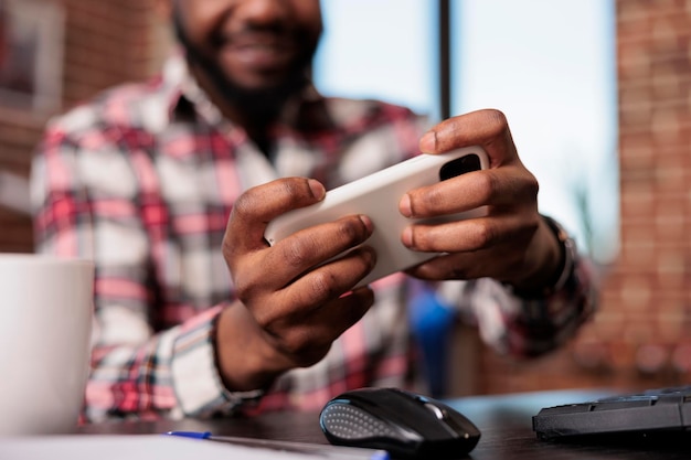 Persona feliz jugando videojuegos en línea con tecnología virtual, sosteniendo un teléfono inteligente para divertirse con el juego en Internet. Disfrutando de la competencia de juegos con el teléfono móvil, trabajando de forma remota. De cerca.