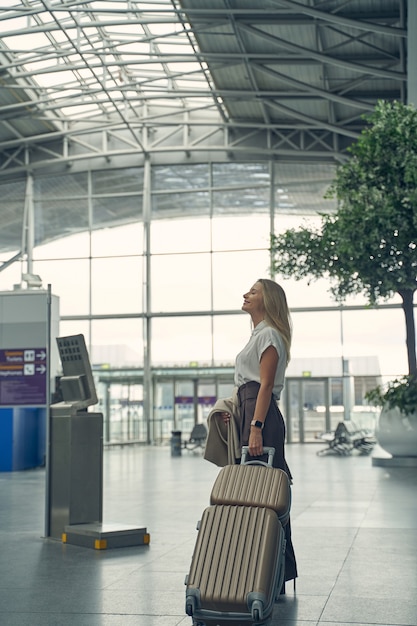 Persona femenina atenta manteniendo el equipaje en la mano izquierda mientras está en el aeropuerto, de pie en posición semi