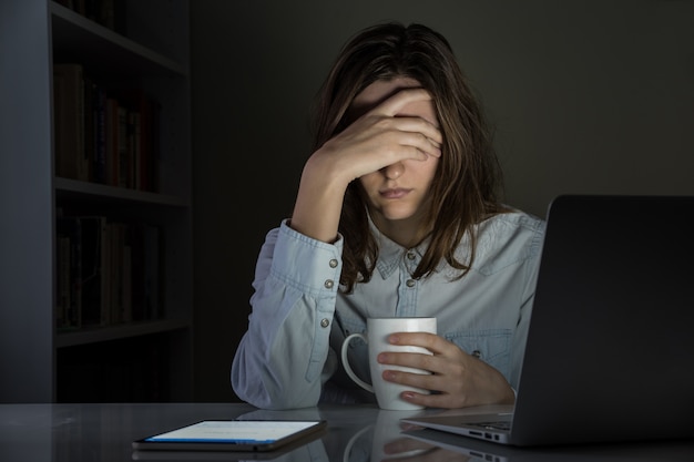 Persona femenina cansada y decepcionada en el lugar de trabajo de la oficina en casa tarde en la noche