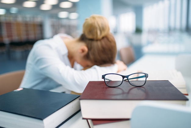 Persona femenina durmiendo en la mesa en la biblioteca.