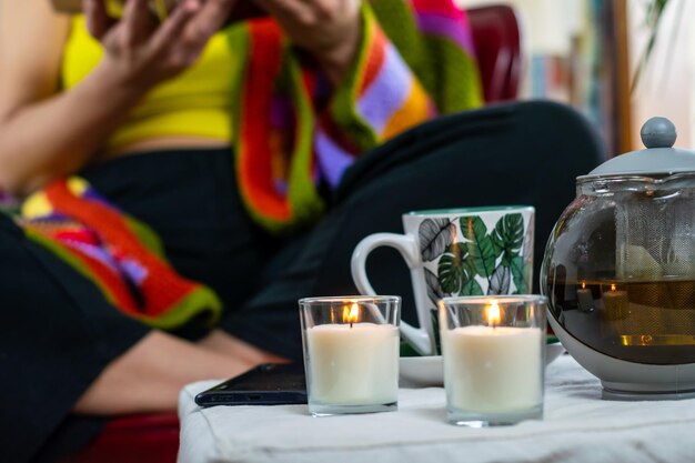 Foto una persona en el fondo con una manta colorida una taza de té y velas