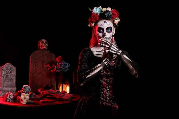 Persona glamorosa con traje de santa muerte en el día de la tradición navideña muerta, posando en el estudio. Modelo con arte corporal de calavera catrina de terror que parece la santa diosa de la muerte.