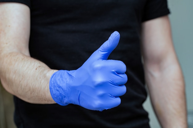 Persona con guantes de látex azules para protección del coronavirus con los pulgares hacia arriba, Covid-19 auto aislamiento o cuarentena en el hogar médicos y enfermeras de apoyo