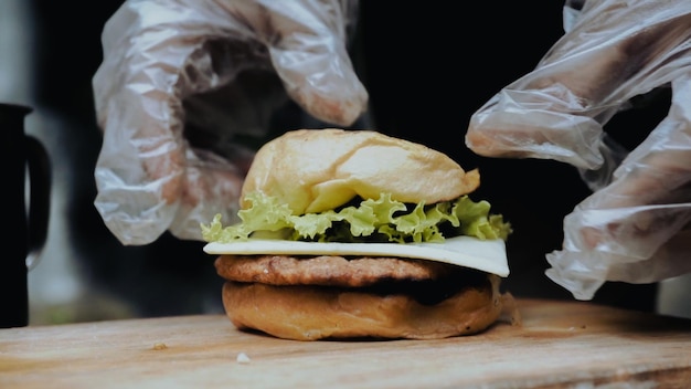 Una persona con guantes pone una hamburguesa en una tabla de madera.