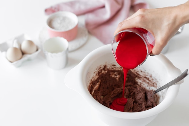 Persona haciendo pastel de terciopelo rojo y agregando colorante alimentario rojo a la masa