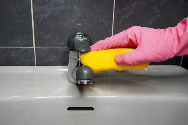 Una persona haciendo tareas domésticas en el baño limpiando el grifo de agua.