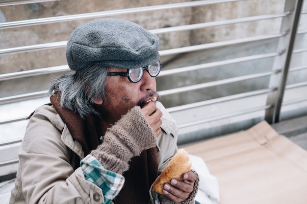 Persona sin hogar sucio sentarse y comer pan en el puente