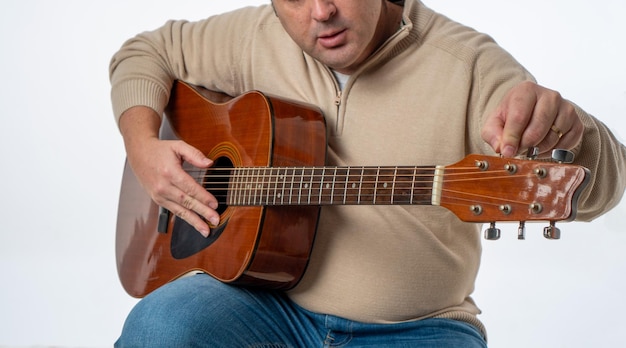 Persona irreconocible afinando la guitarra en una fotografía de estudio de fondo blanco
