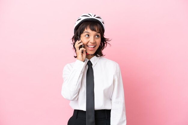 Persona joven con un casco de bicicleta aislado sobre fondo rosa manteniendo una conversación con el teléfono móvil