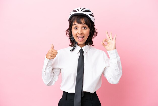 Persona joven con un casco de bicicleta aislado sobre fondo rosa que muestra el signo de ok y el pulgar hacia arriba gesto