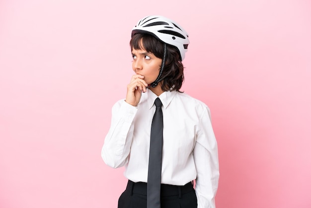 Persona joven con un casco de bicicleta aislado sobre fondo rosa que tiene dudas y con expresión de la cara confusa