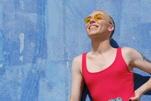 Persona joven no binaria con gafas de sol y sonriendo mientras posa al aire libre en un día soleado. Concepto de identidad de género.