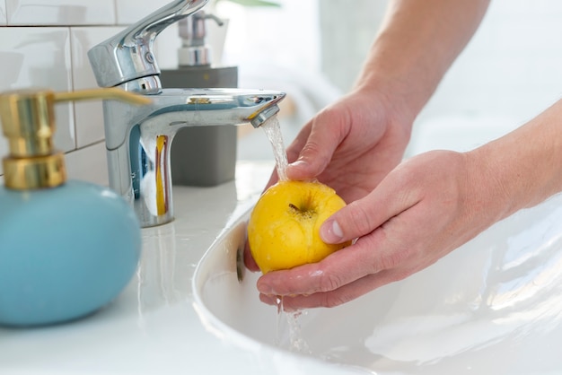 Persona lavando una manzana amarilla en el baño.