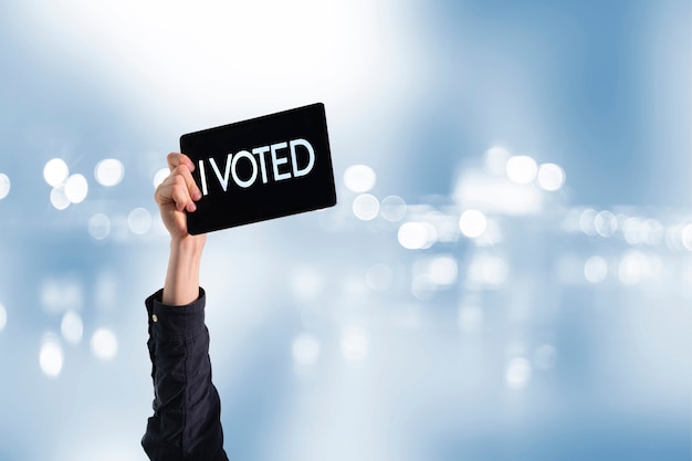 Una persona con una mano levantada con placa negra y texto "yo voté", elección de democracia
