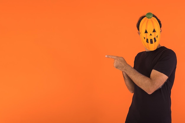 Persona con máscara de calabaza celebrando Halloween apuntando hacia un lado con los dedos sobre fondo naranja Concepto de celebración del Día de los Difuntos y el Día de Todos los Santos