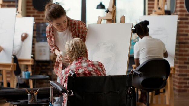 Persona mayor en silla de ruedas dibujando un modelo de inspiración en la clase de arte, creando bocetos modernos para desarrollar nuevas habilidades artísticas. Taller adaptado para personas con discapacidad para dibujar obras de arte con lápiz y herramientas.