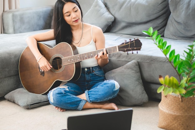 Persona mujer tocando instrumento musical de guitarra acústica en casa, estilo de vida de chica joven músico asiático