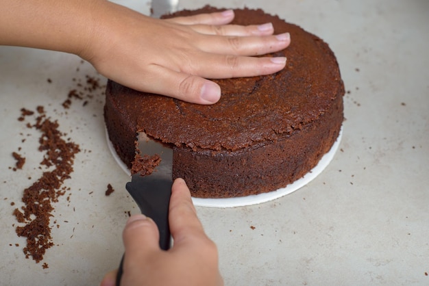 Persona nivelando un pastel con un cuchillo Pastel de chocolate sin decoración en una mesa de madera