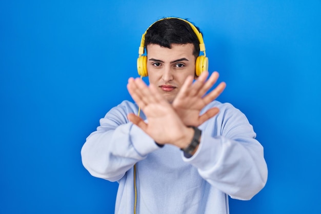Persona no binaria escuchando música usando auriculares expresión de rechazo cruzando los brazos y las palmas haciendo signo negativo cara enojada