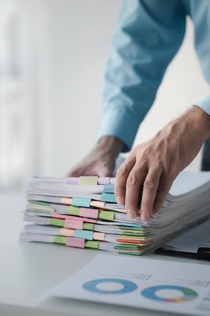 Foto una persona en una oficina con una gran pila de papeles, es un empleado de la empresa que gestiona el papeleo y archiva las finanzas corporativas. concepto de gestión de documentos.