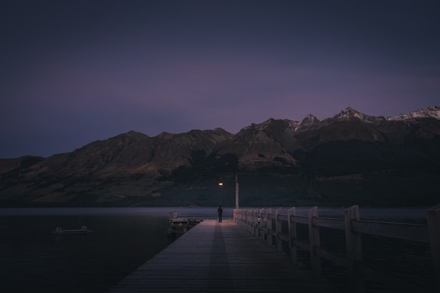 Foto persona de pie al final del muelle en el lago