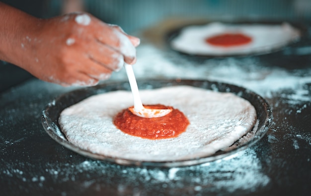 Persona poniendo salsa en pizza casera