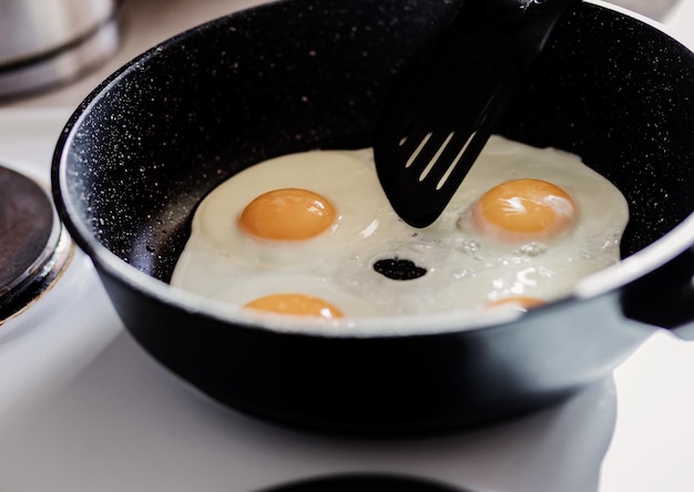 Persona preparando huevos fritos en sartén para desayunar