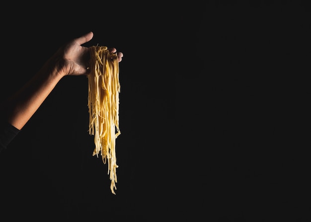 Persona de primer plano sosteniendo fideos con fondo oscuro