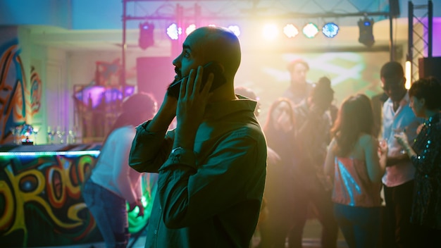 Foto persona que contesta una llamada telefónica en la discoteca, tratando de tener una conversación remota en la fiesta disco. hombre hablando por teléfono inteligente, disfrutando de la noche en el evento con música funky. disparo de mano.