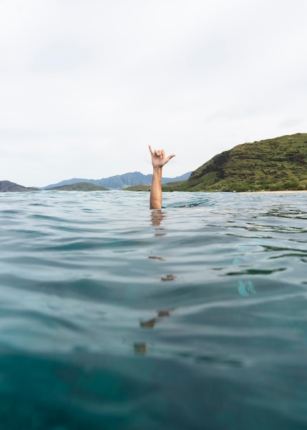 Persona que muestra el gesto de la mano mientras está sumergido bajo el agua