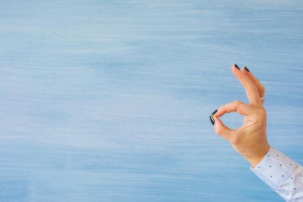 Persona que muestra el gesto de la mano ok sobre fondo azul vacío