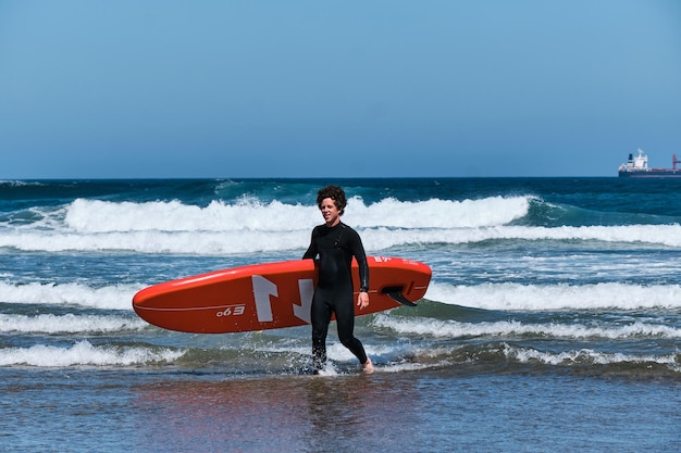 Persona que practica surf que sale del mar que sostiene su tabla de surf