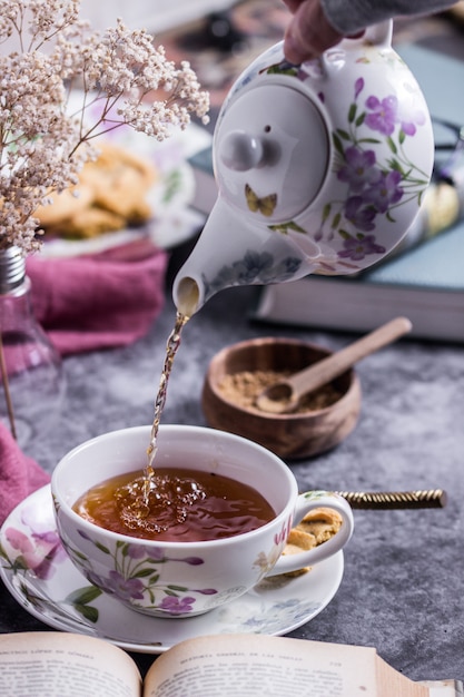 Una persona que sirve el té con una hermosa tetera mientras lee un libro