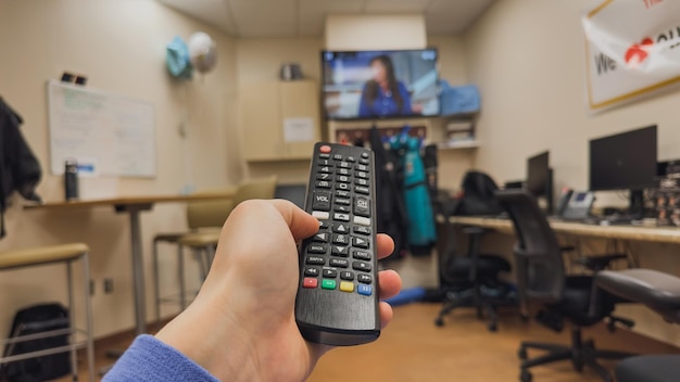 Foto una persona que sostiene un control remoto en una habitación con una televisión de fondo.