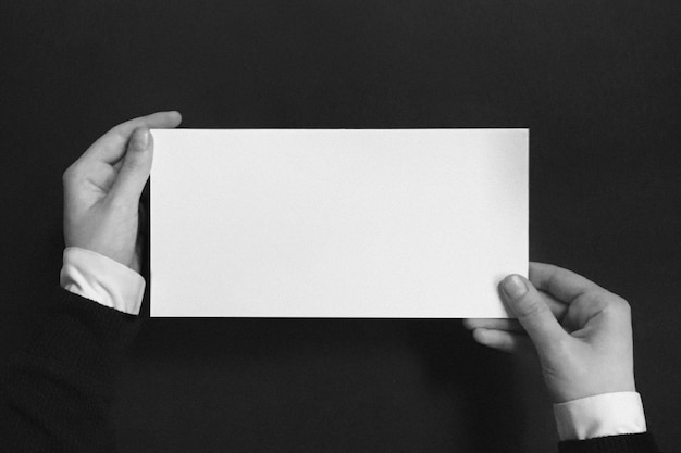 Una persona que sostiene una maqueta de un sobre blanco vacío con un fondo oscuro.