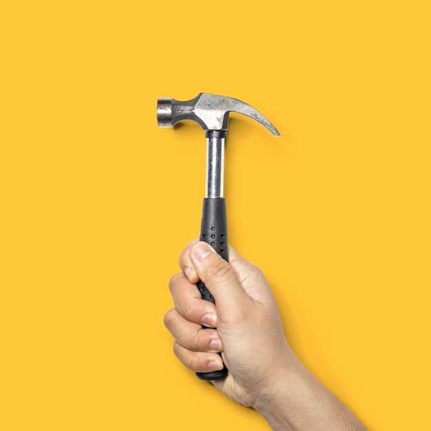 Persona que sostiene un pequeño martillo con mango negro, el martillo es una herramienta para clavos de martillo, aislado sobre fondo amarillo y trazado de recorte.