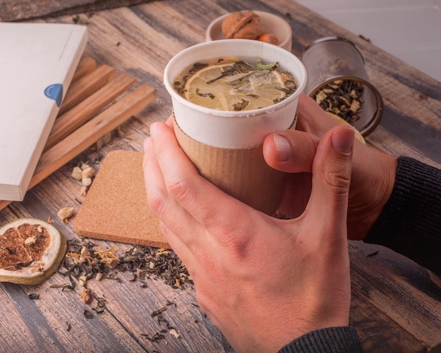 Una persona que sostiene una taza de té con una rodaja de limón y un libro sobre la mesa